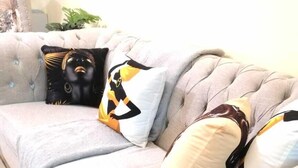 Un sofá con textura y almohadones decorativos, un tapete estampado y una planta al fondo.