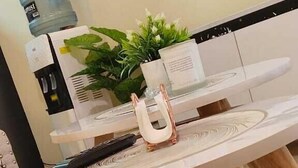 Una mesa de comedor redonda con superficie blanca y patas de madera, acompañada por una planta en maceta y un florero decorativo.
