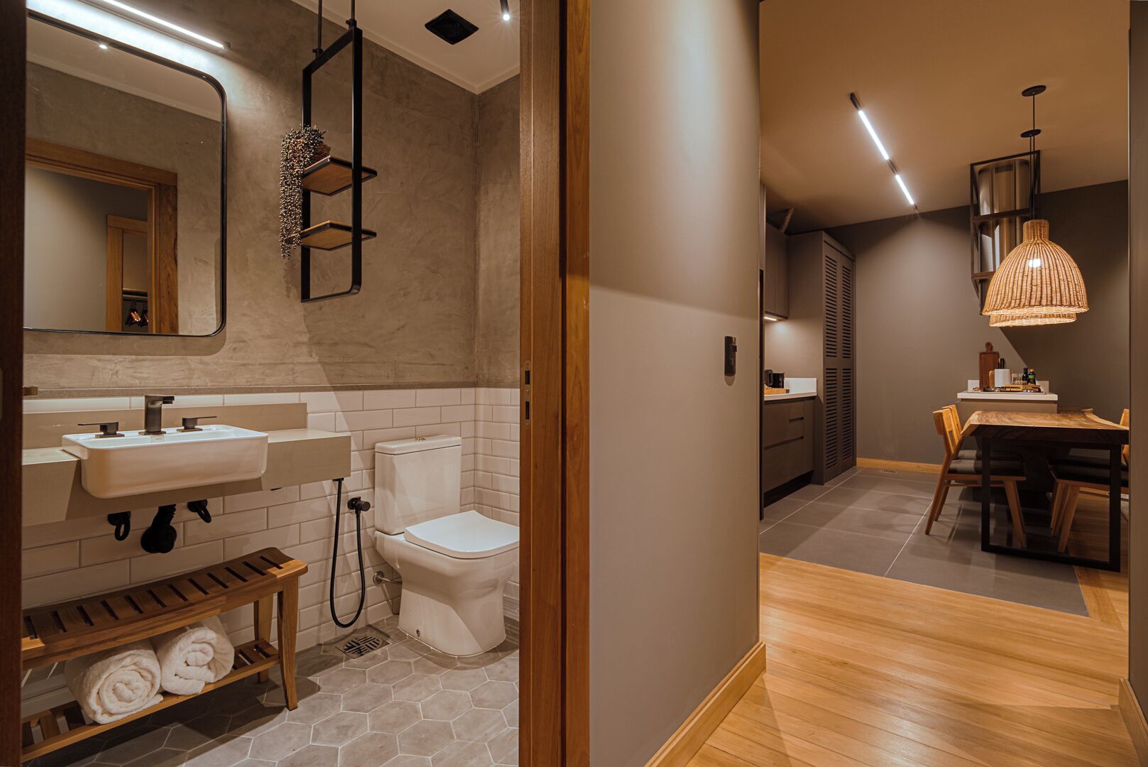 A modern bathroom with a white sink, toilet, and wooden shelf with towels.