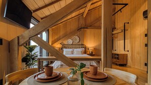 A wooden interior with a dining table set for two, a bed with a wooden headboard, and a large window providing natural light. - Mater Hotel (Canela)