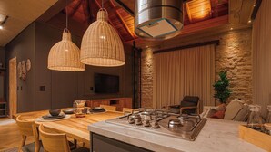 A modern kitchen with a central island, wooden dining table, wicker pendant lights, and a stone accent wall. - Mater Hotel (Canela)