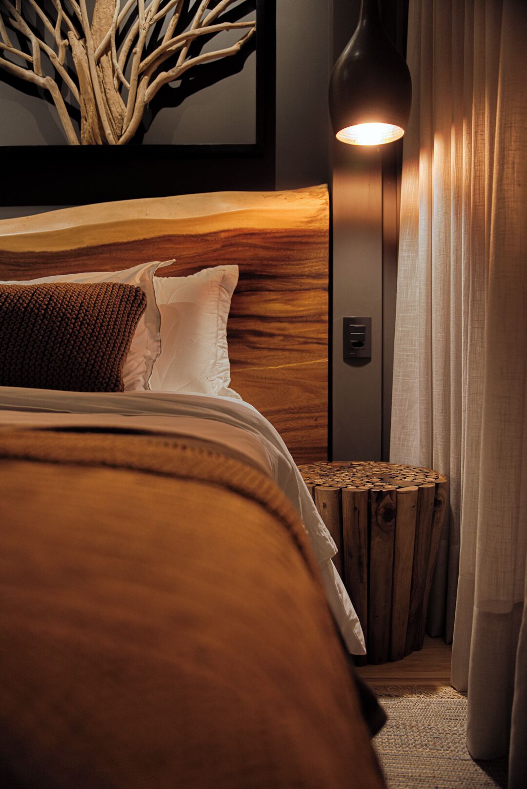 Una cama bien hecha con cabecera de madera, una lámpara de noche y una mesita de noche de fibras trenzadas.