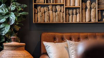 A room with a brown leather sofa, a large wooden sculpture wall, and a large green plant.