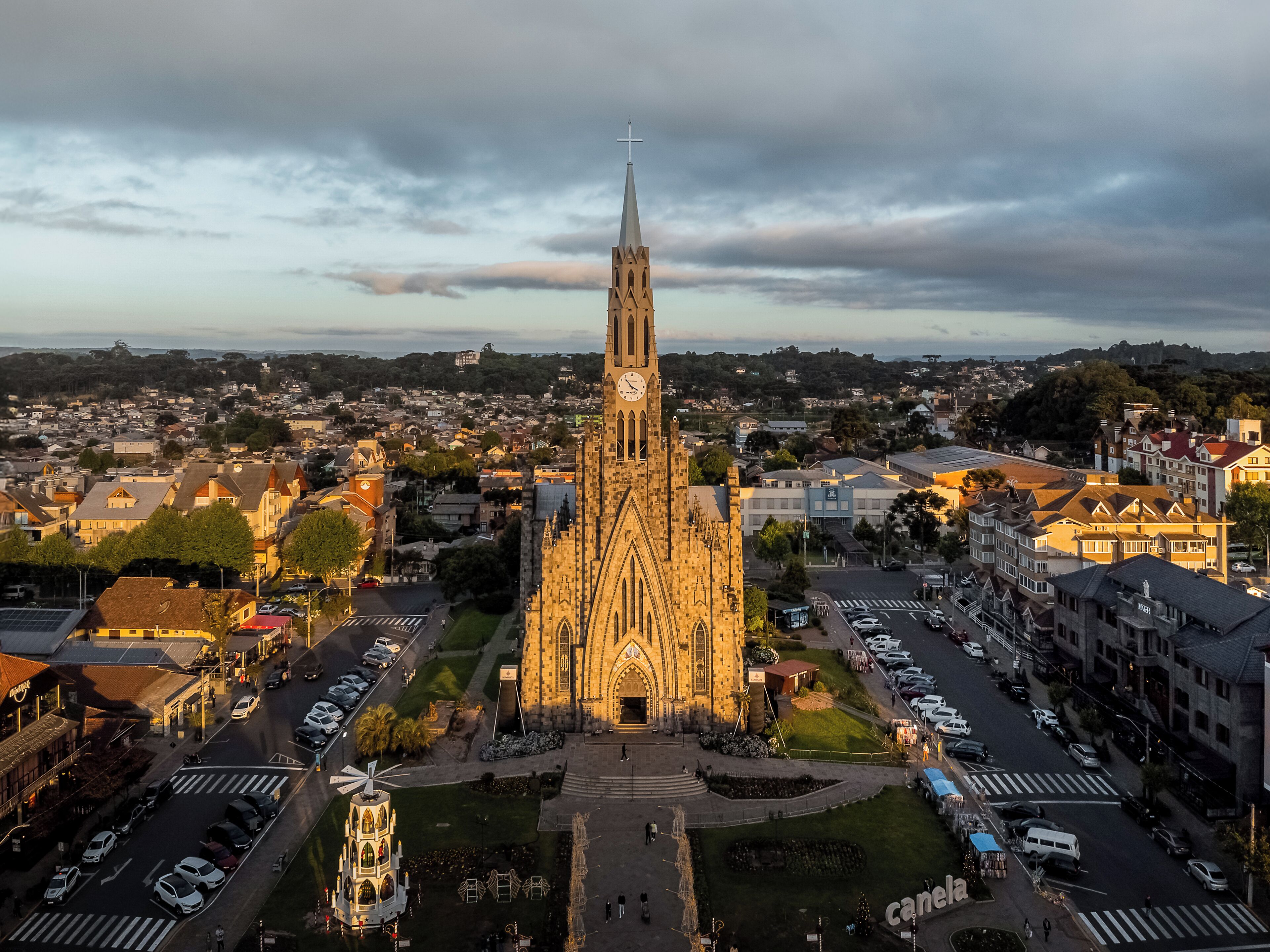 A large church with a tall spire, surrounded by a parking lot and a small plaza with a windmill.