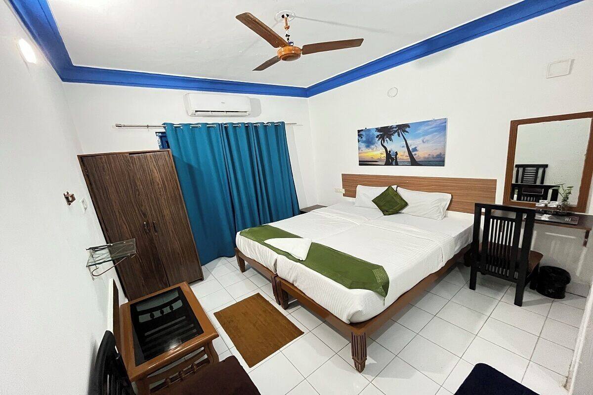 Une chambre à coucher comprenant un lit, un bureau, une chaise, un ventilateur de plafond, une fenêtre avec des rideaux et un tableau accroché au mur.