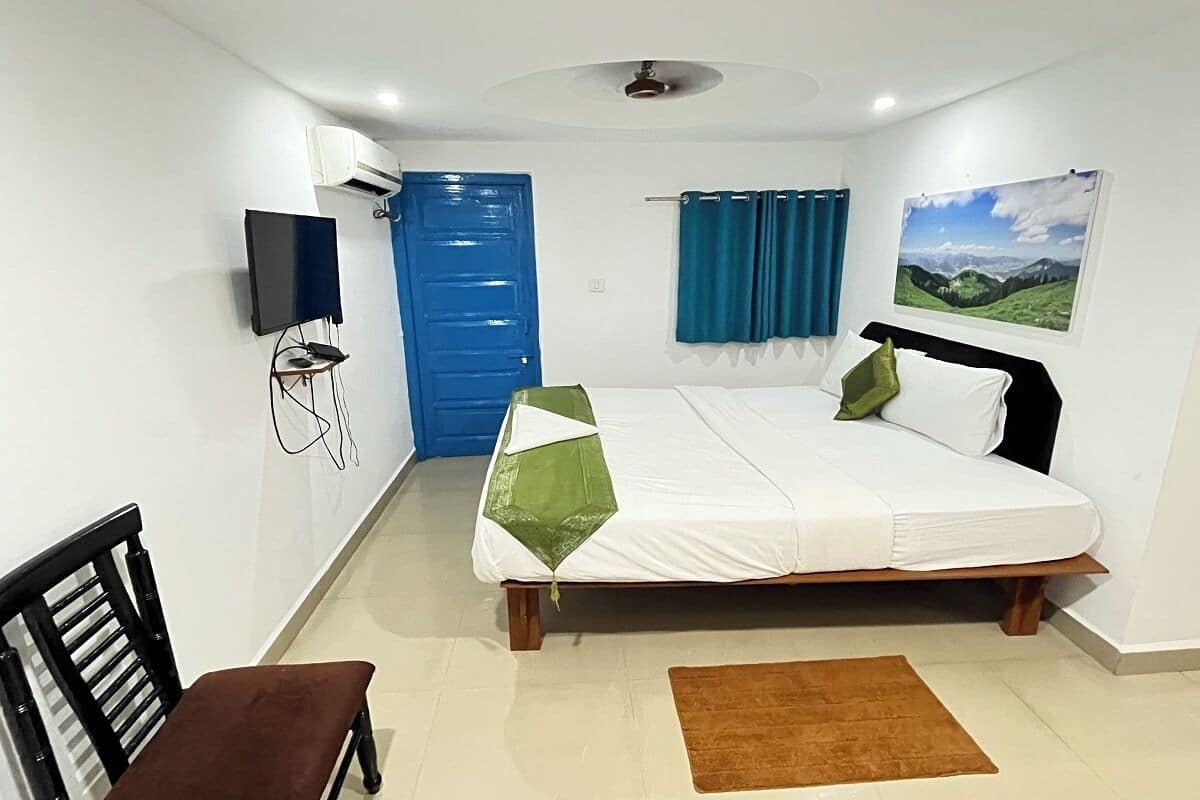 Une chambre à coucher avec un lit, un téléviseur fixé au mur, une porte bleue et un tableau représentant un paysage.