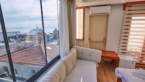Habitación de hotel con un amplio ventanal, un sofá, una mesa de madera y un equipo de aire acondicionado.