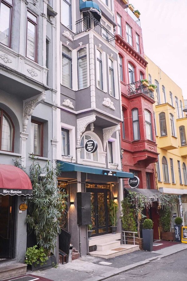 A row of multi-story buildings with distinct architectural styles, including a corner building with a balcony and a storefront with a sign.
