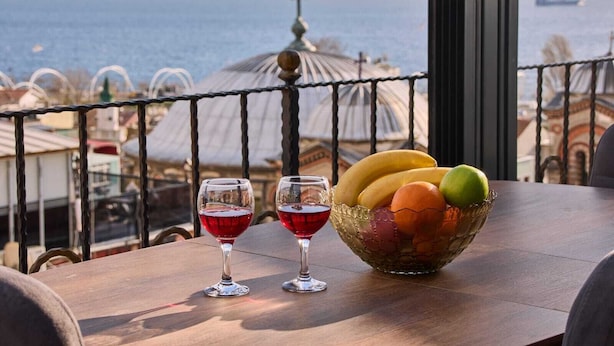 Una mesa con dos copas de vino y un frutero en un balcón con vista al mar.