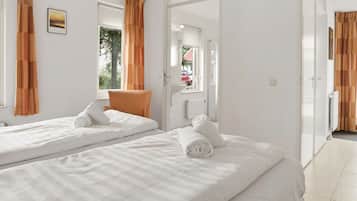 A hotel room with two beds, a chair, a bathroom, and a view of the outside.