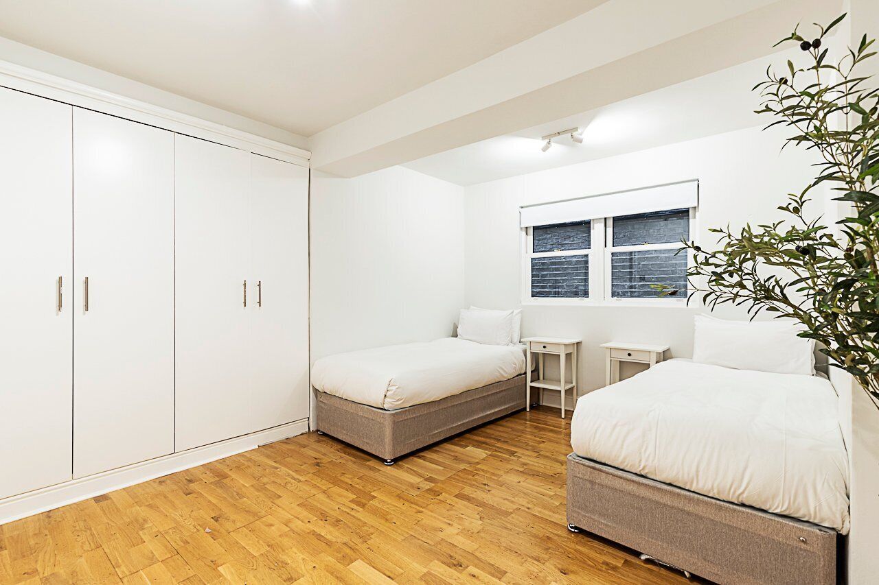 Une chambre avec deux lits, une armoire, une petite table et une fenêtre avec des stores.