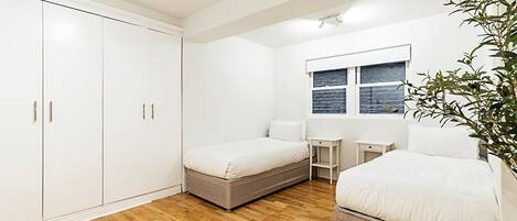 Une chambre avec deux lits, une armoire, une petite table et une fenêtre avec des stores.