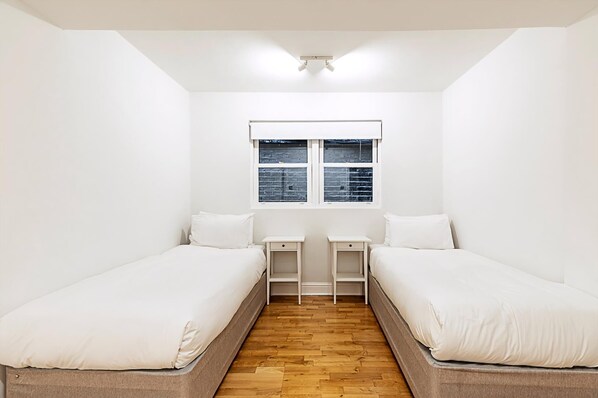 A small, clean room with two single beds, a window, and a wooden floor.