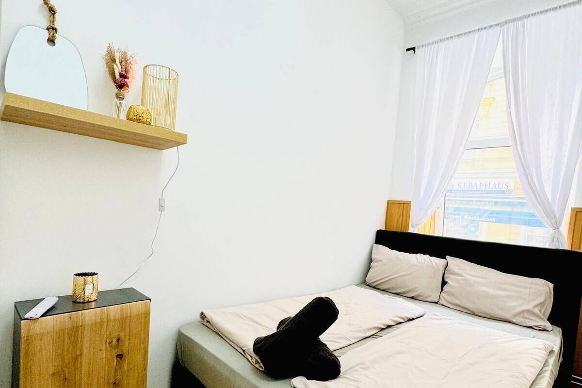 A bedroom with a bed, a wooden nightstand, a mirror, and a window with curtains.