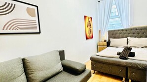 A modern bedroom with a grey sofa, a bed with a tufted headboard, and a framed abstract painting on the wall. - 10 Economy Rooms-Shared Bath & Kitchen (Vienna)
