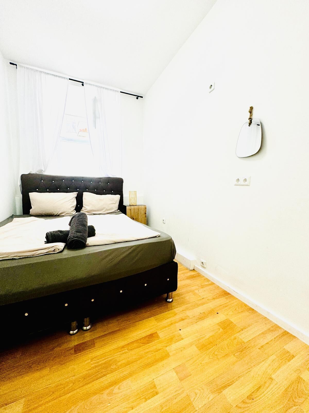 Ein Schlafzimmer mit einem Bett, Holzboden, einer Wandgitarre und einem Fenster mit Vorhängen.