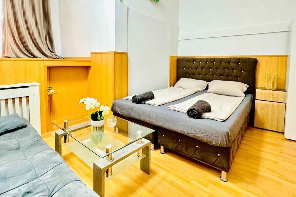 A modern hotel room with a single bed, a sofa, a glass coffee table, and a wooden floor.