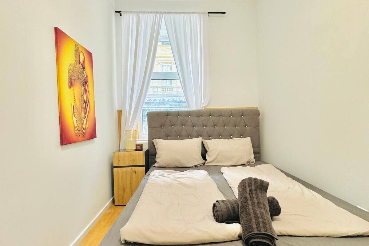 A modern bedroom with a large bed, a nightstand, a lamp, and a window with curtains.