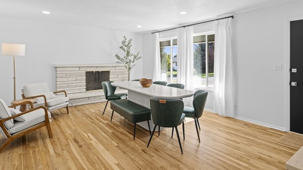 A modern dining area with a wooden floor, white walls, and a fireplace. There are four chairs and a table with a bowl. - Retro Retreat Newly Renovated in SoJo (South Jordan)