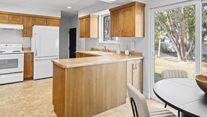 A modern kitchen with wooden cabinets, a white refrigerator, and a large island. - Retro Retreat Newly Renovated in SoJo (South Jordan)