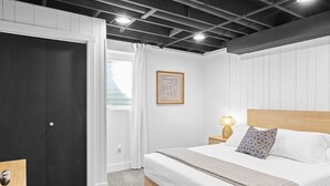 A modern bedroom with a large bed, a nightstand, a wall-mounted lamp, and a door leading to another room. - Retro Retreat Newly Renovated in SoJo (South Jordan)