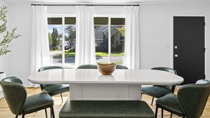 A dining area with a white table, green upholstered chairs, and a wooden bowl centerpiece. - Retro Retreat Newly Renovated in SoJo (South Jordan)