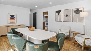 A modern dining area with a white table, green upholstered chairs, and a wooden bowl centerpiece. - Retro Retreat Newly Renovated in SoJo (South Jordan)