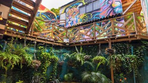 En storslagen atrium med en takkonstruktion i trä, frodiga gröna växter och en färgstark väggmålning.
