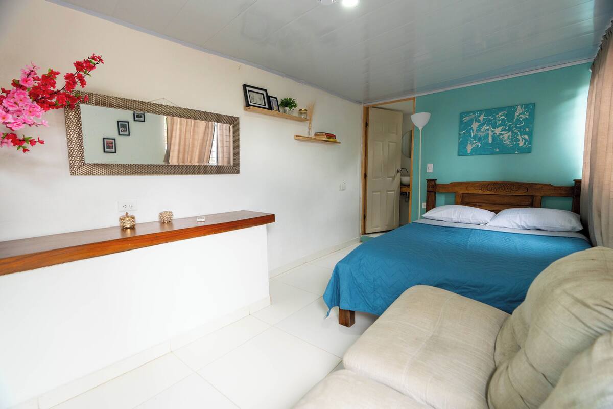Un dormitorio con cama, mesita de noche, espejo, cómoda, silla y puerta.