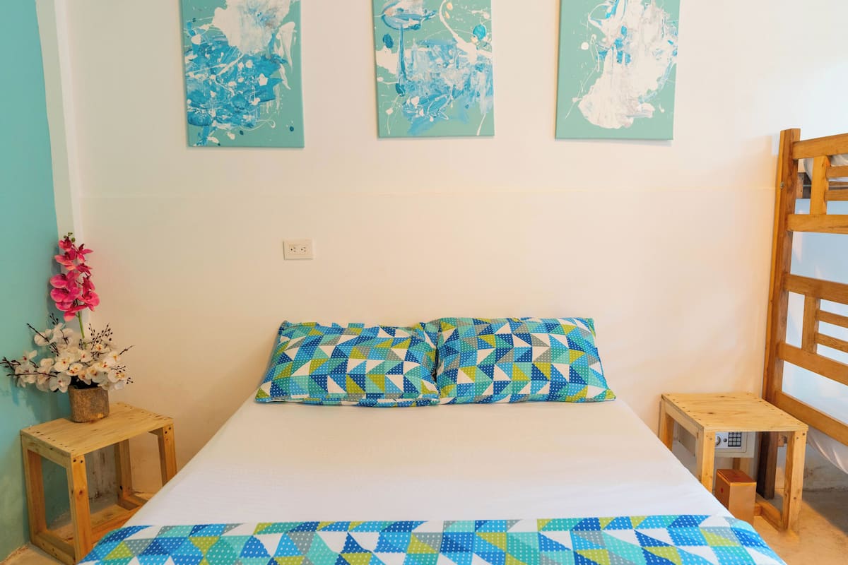 Un dormitorio con una cama, dos mesitas de noche, una silla de madera y tres cuadros abstractos en la pared.