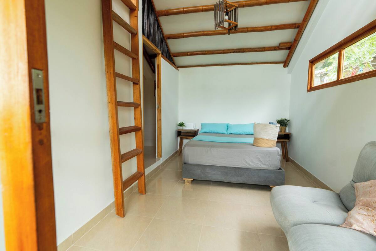 Una habitación pequeña con cama, sofá, escalera y ventana.