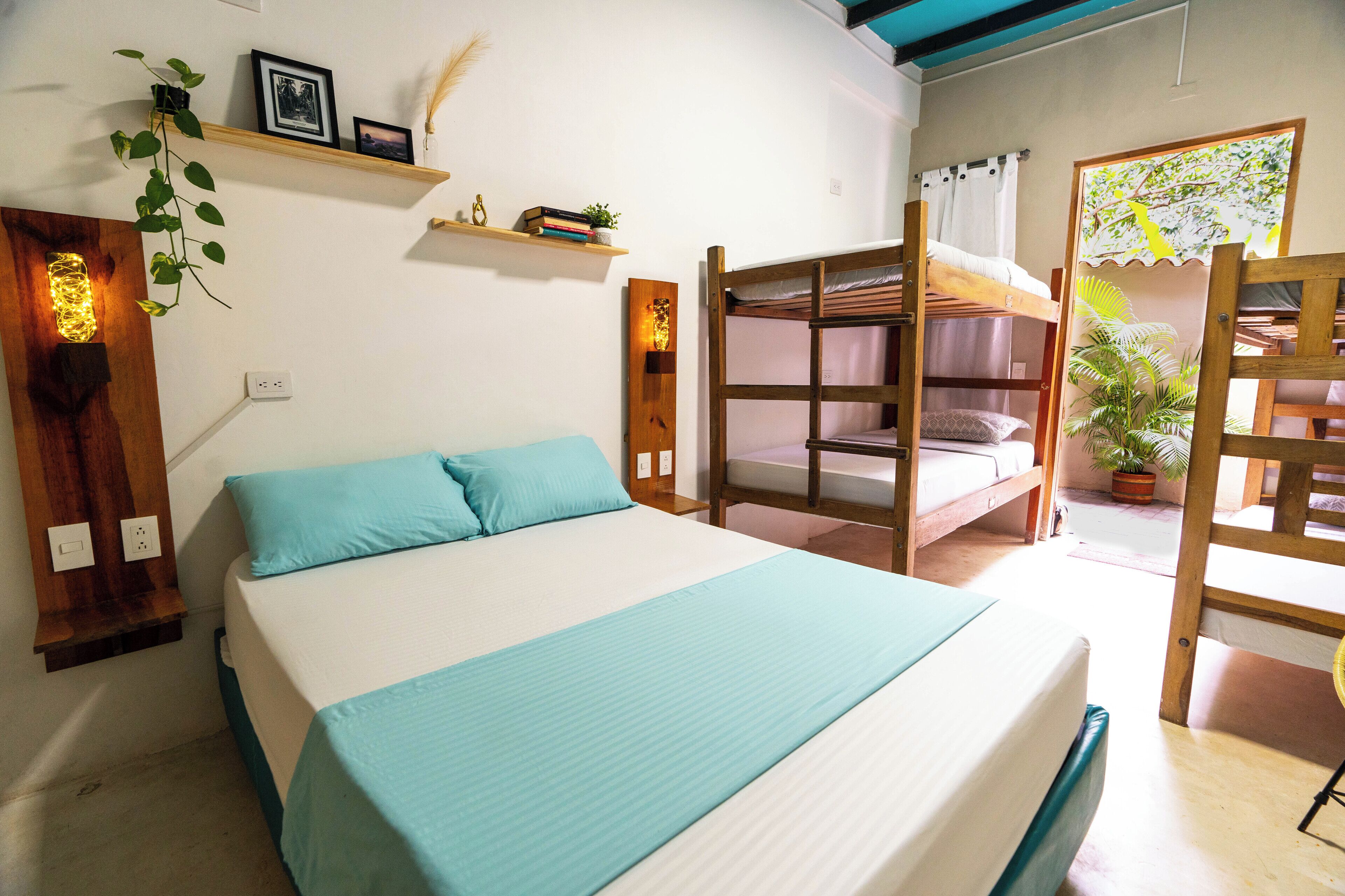 Un dormitorio con una cama litera, una cama individual, un estante con libros y plantas, y una lámpara fijada a la pared.