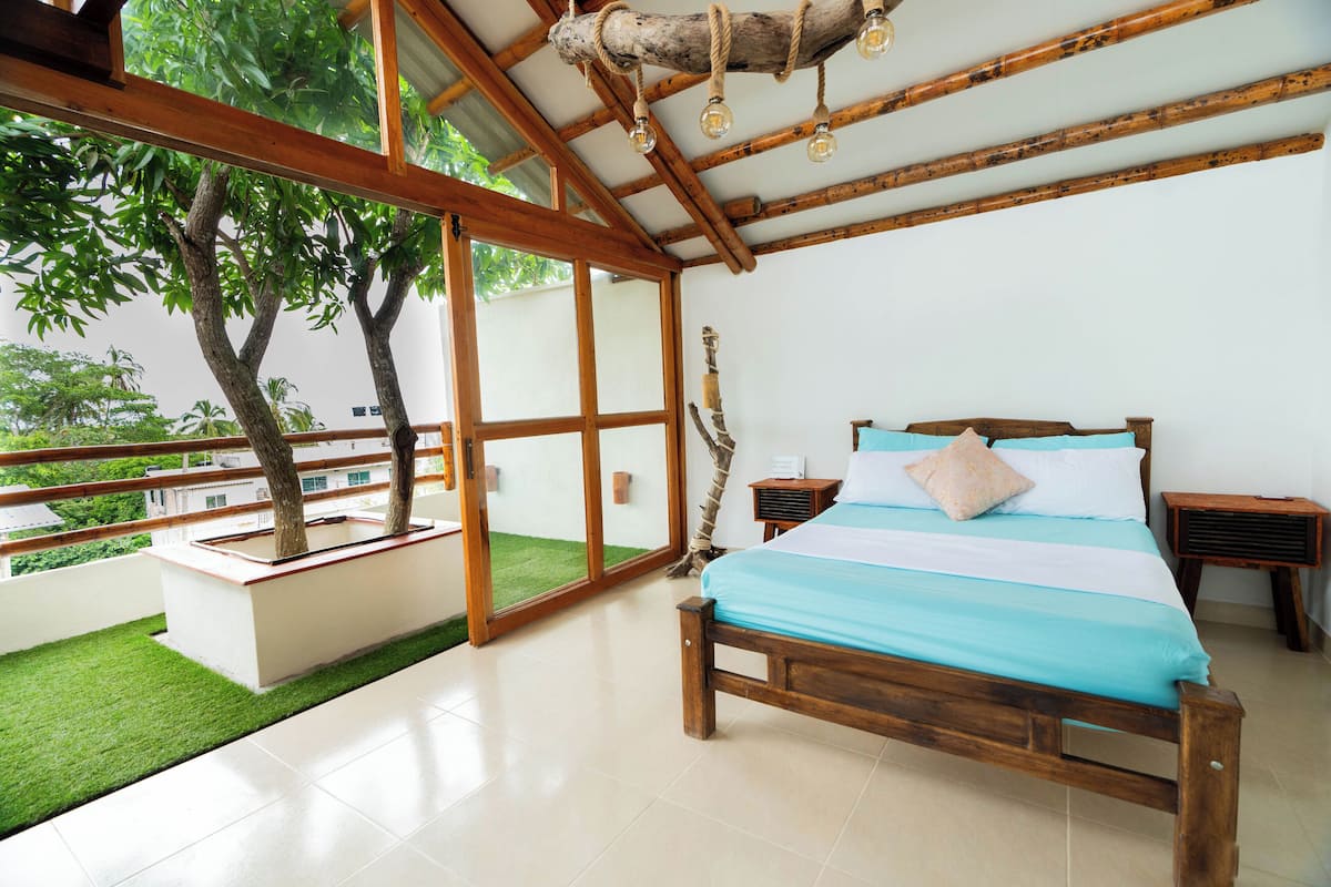 Un dormitorio espacioso con una cama grande, cabecera de madera y vistas a un jardín exuberante a través de amplios ventanales correderas.