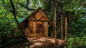 Una cabaña de madera con techo inclinado, rodeada de un bosque denso.