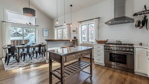 A modern kitchen with wooden flooring, a central island, pendant lighting, and a stainless steel stove.