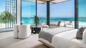 Een moderne slaapkamer met een groot bed, twee fauteuils, een tafeltje en uitzicht op zee.
