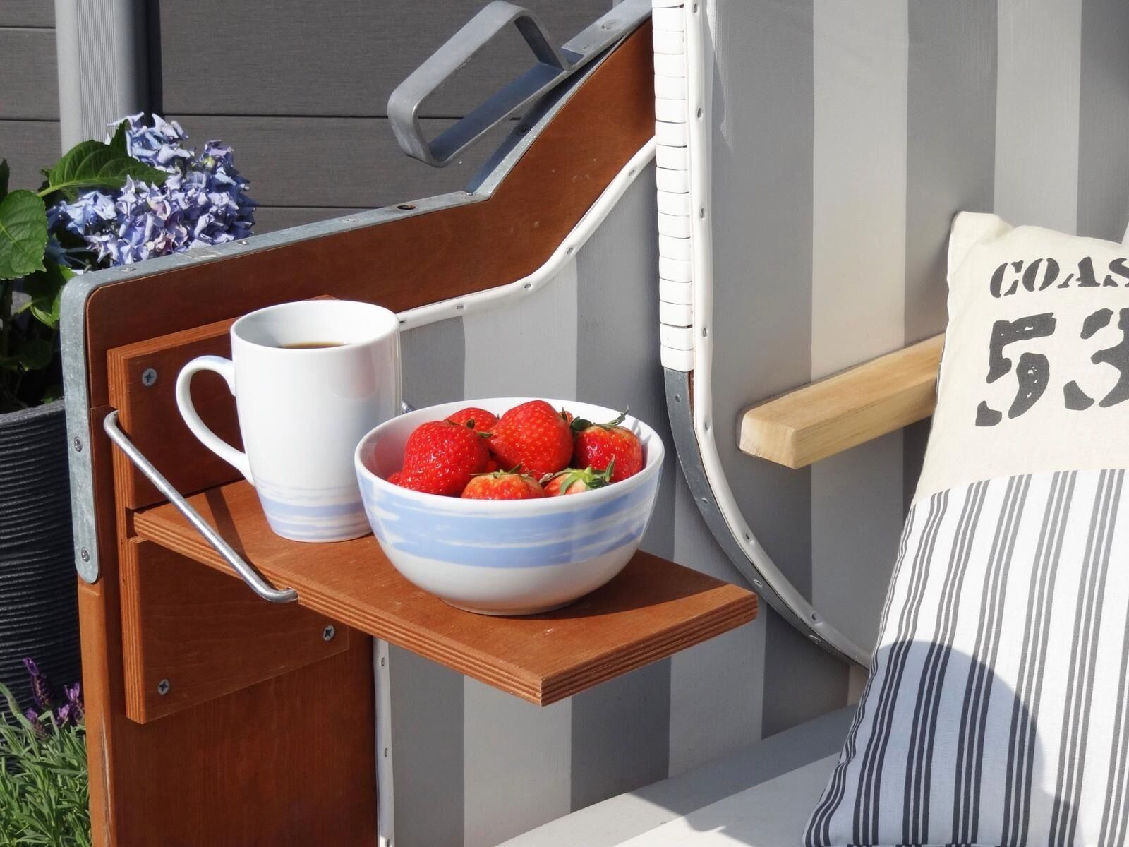 Un coin salon extérieur accueillant, avec un banc en bois, une tasse blanche et un bol de fraises.