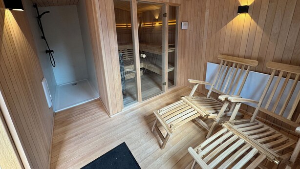Uma sala de sauna com paredes e bancos de madeira, uma porta de vidro para uma sala de vapor e um tapete preto no chão.