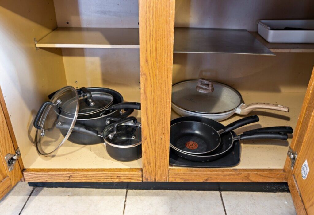 A kitchen cabinet with a stove, pots, and pans.
