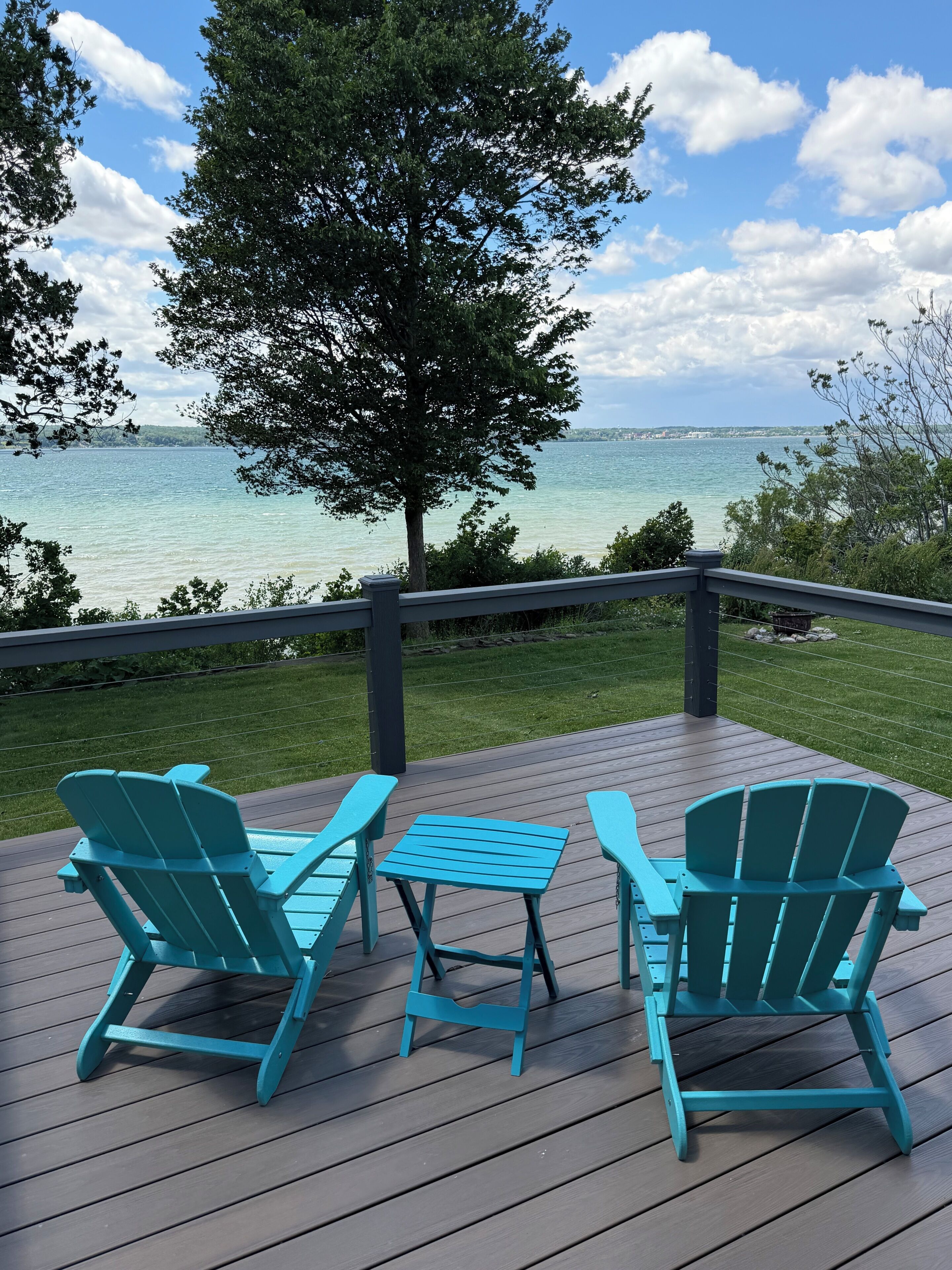 A deck with two chairs and a table, overlooking a body of water and a tree.