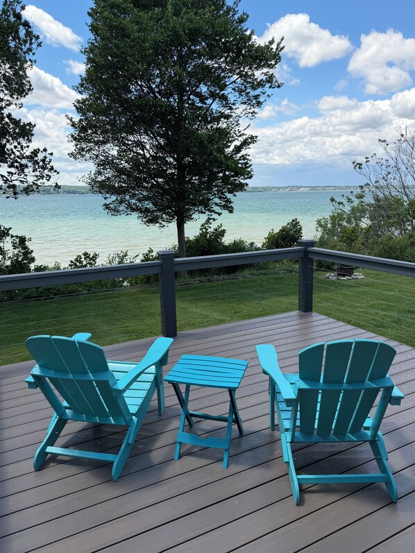 A deck with two chairs and a table, overlooking a body of water and a tree.