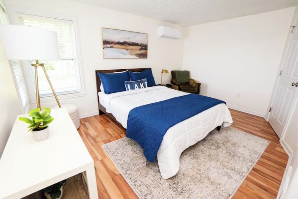 A bedroom with a bed, bedside table, lamp, chair, and a painting on the wall.