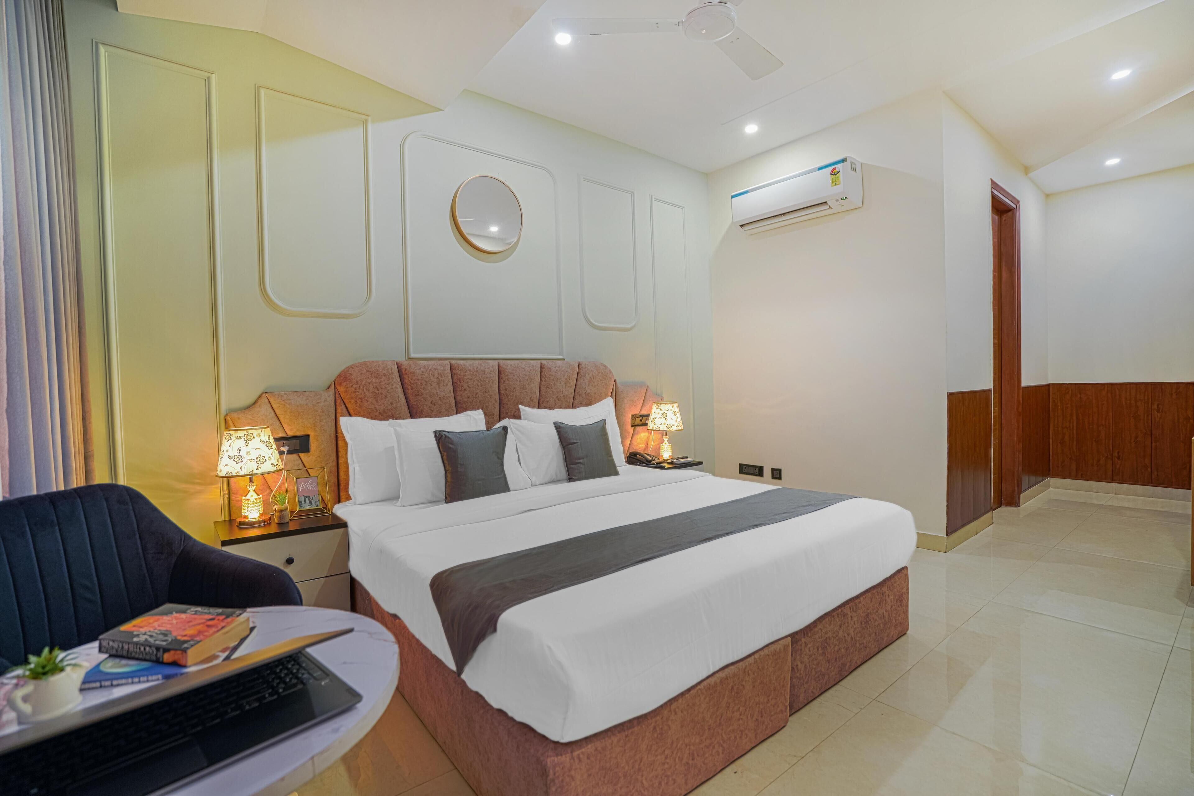 Una habitación de hotel moderna con una cama grande, lámparas de noche, un escritorio con una computadora portátil y un equipo de aire acondicionado.