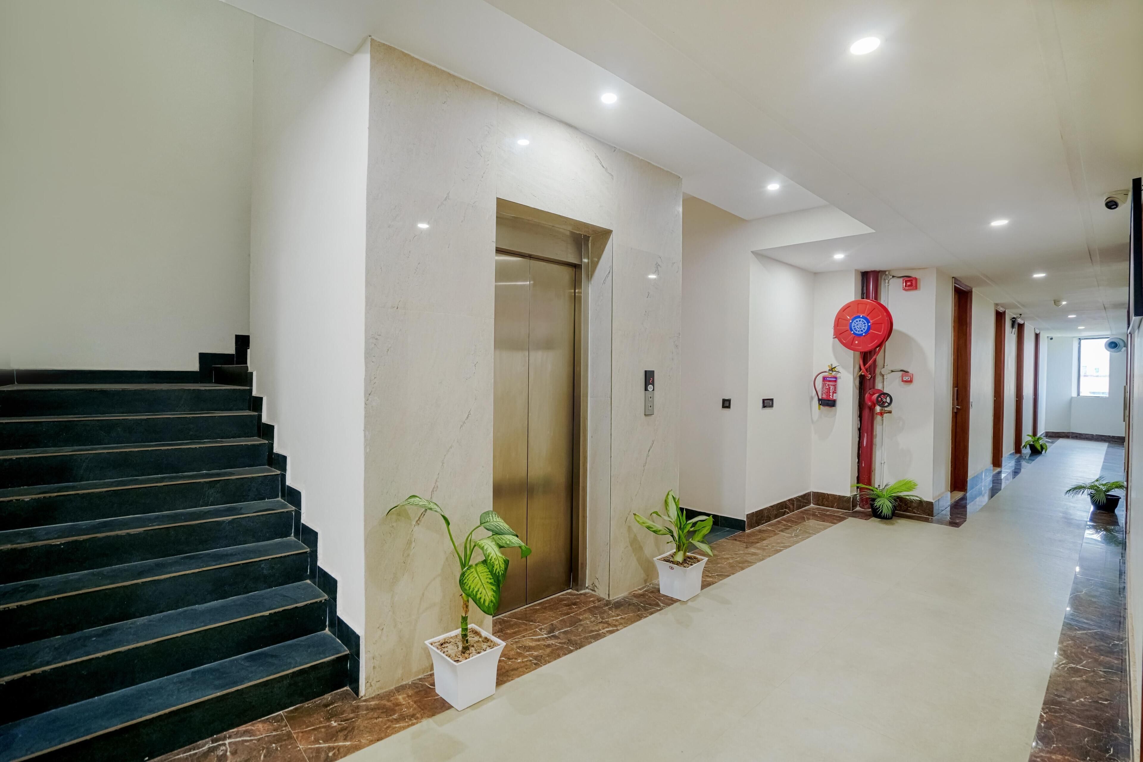 Un moderno vestíbulo de hotel con una escalera de mármol, un ascensor, plantas en macetas y un ventilador rojo.