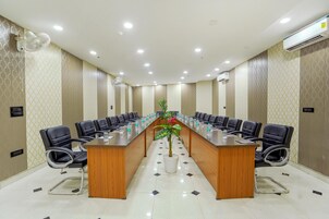 Un salón de conferencias con una larga mesa de madera, sillas negras y una planta en maceta.
