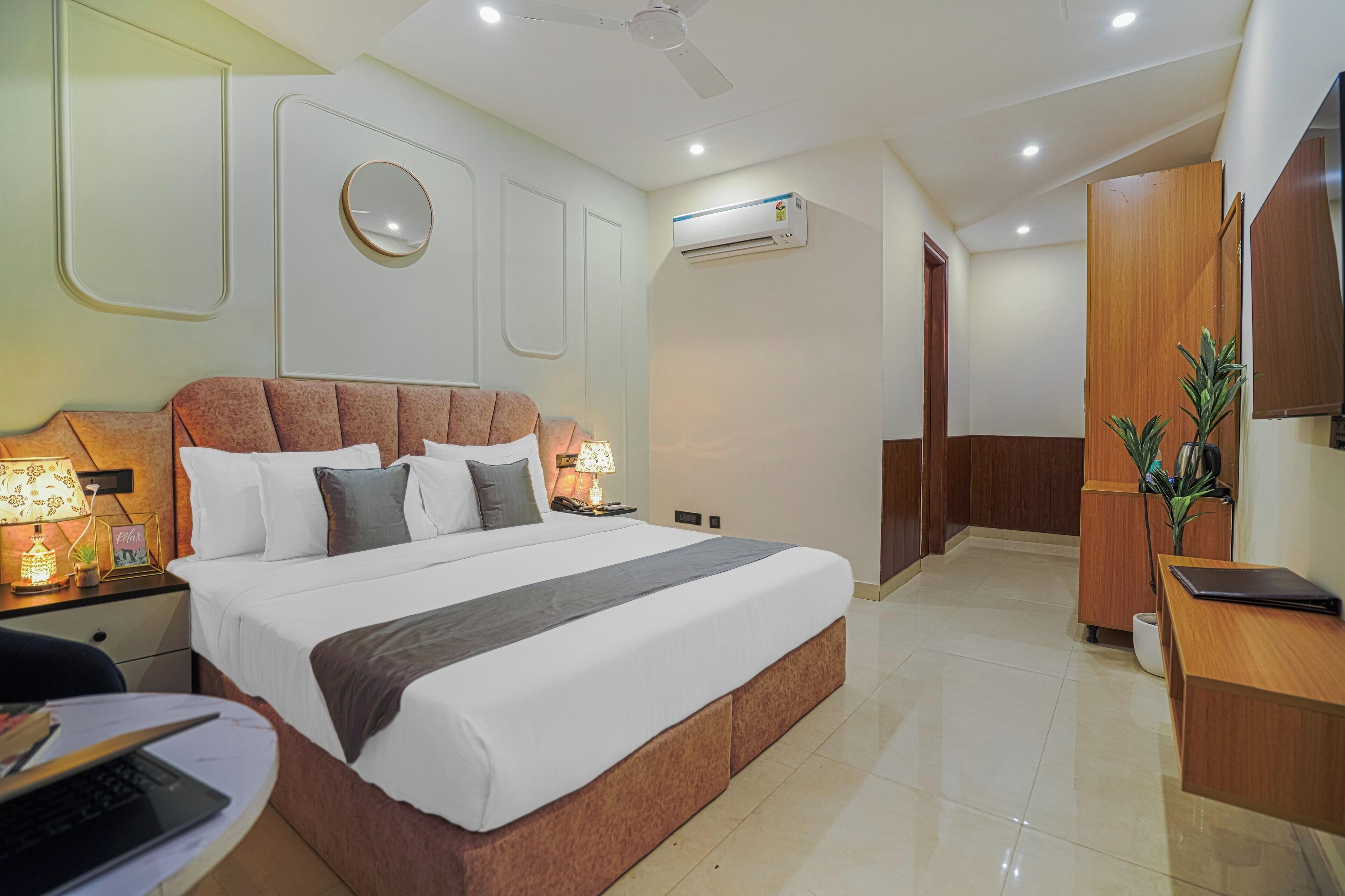 A hotel room with a large bed, bedside lamps, a desk with a laptop, and a TV.
