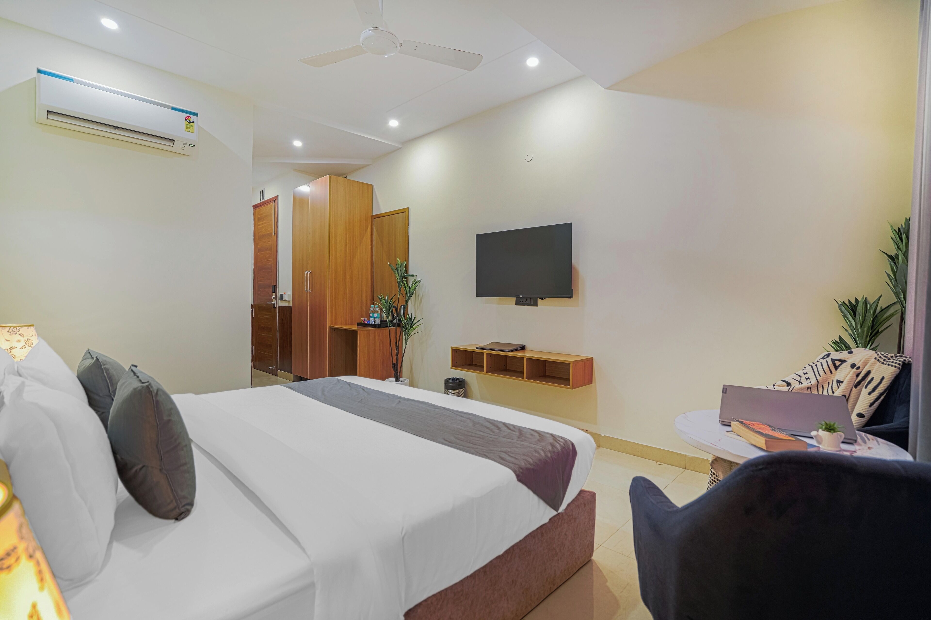 Een moderne hotelkamer met een bed, een bureau met een laptop, een televisie en een plafondventilator.