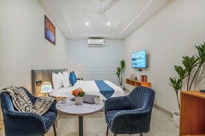 A modern hotel room with a bed, two armchairs, a small table with a lamp, a TV, and a plant. - Hotel Sky View - Zirakpur, Chandigarh (Dera Bassi)
