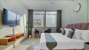 A hotel room with a large bed, a TV mounted on the wall, a small table with chairs, and a window with curtains. - Hotel Sky View - Zirakpur, Chandigarh (Dera Bassi)