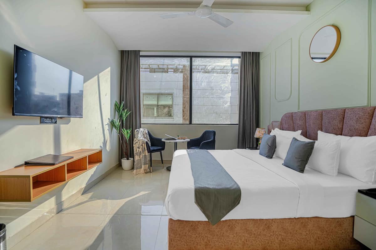A hotel room with a large bed, a TV mounted on the wall, a small table with chairs, and a window with curtains.